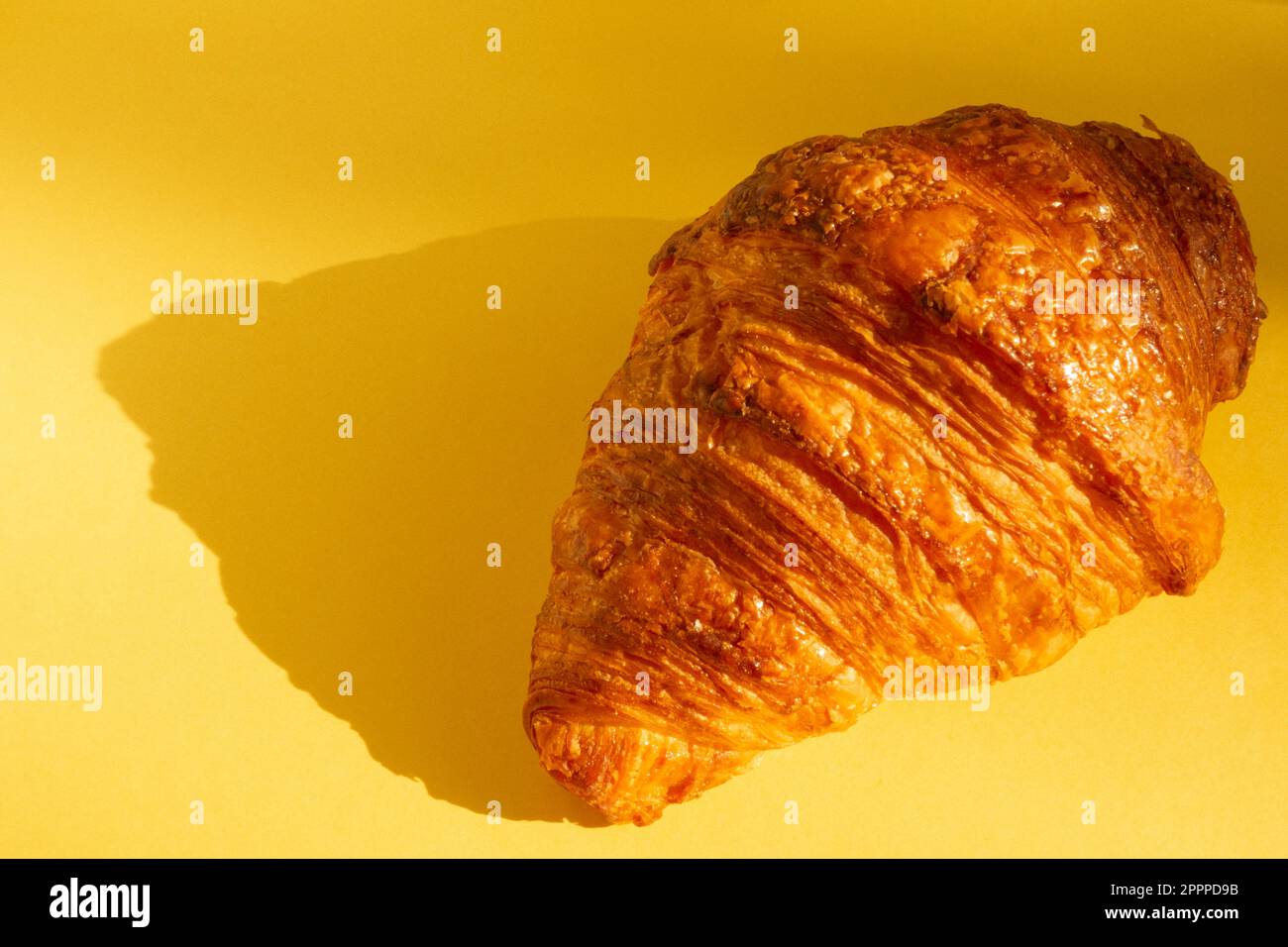 Vista ravvicinata di un croissant francese appena sfornato su sfondo giallo con luce solare Foto Stock