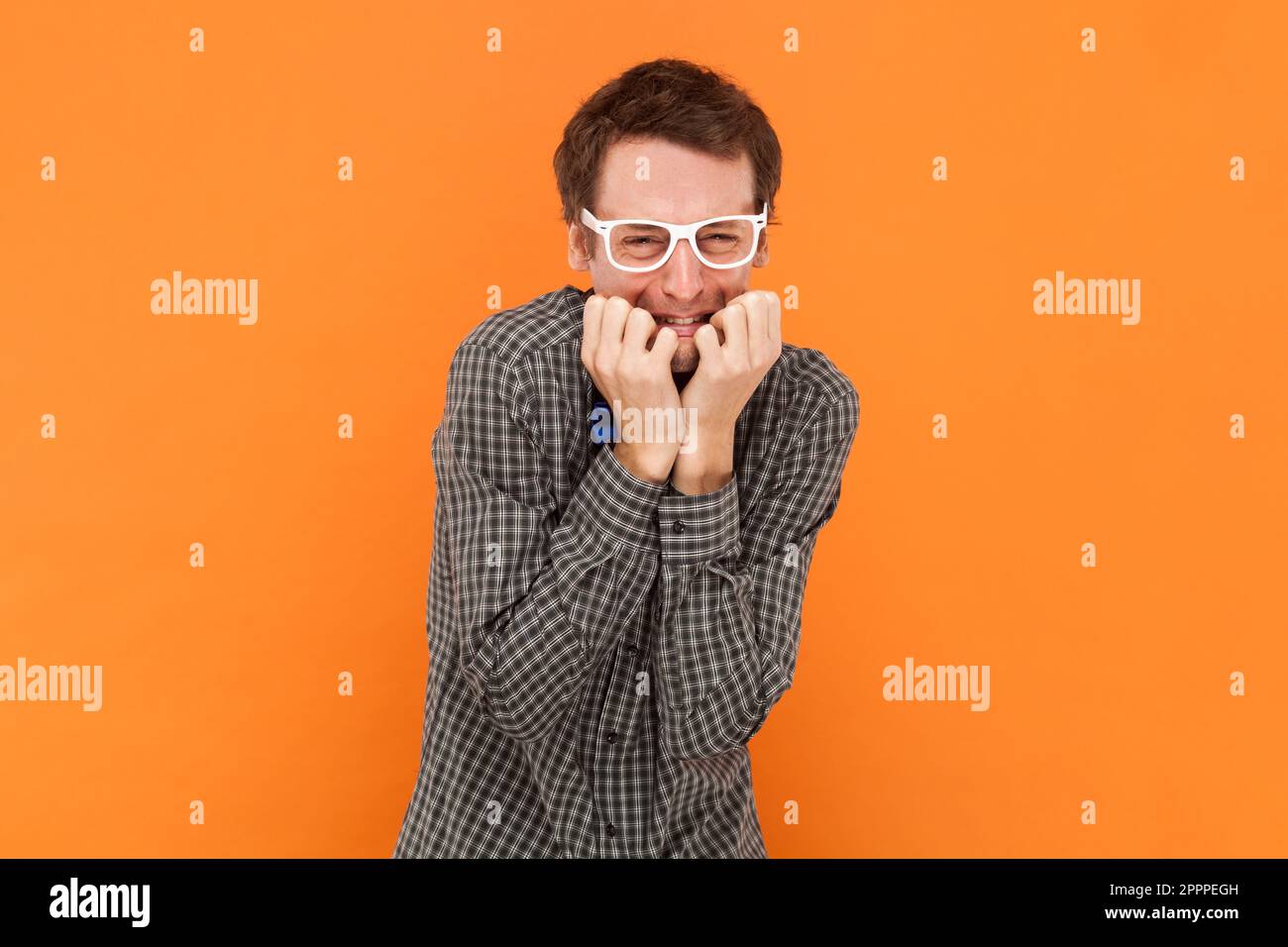 Ansioso uomo perplesso nerd morde unghie dita stand insicuro e nervoso, si sente a disagio, indossando camicia con cravatta blu arco e occhiali bianchi. Studio al coperto isolato su sfondo arancione. Foto Stock