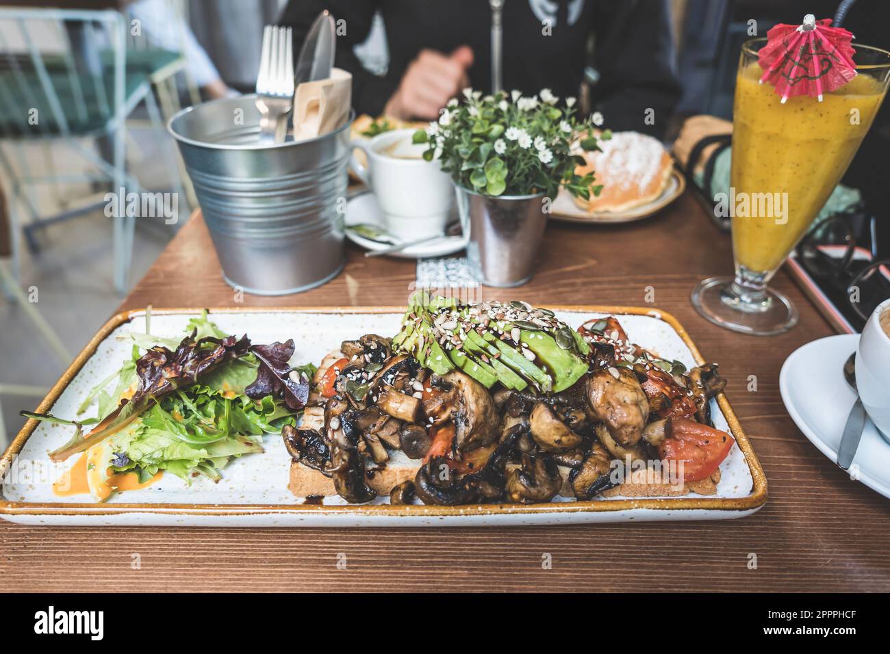 Focalizzazione selettiva su un panino con funghi, avocado, lattuga e semi serviti con bevande su un tavolo in legno in un ristorante Foto Stock