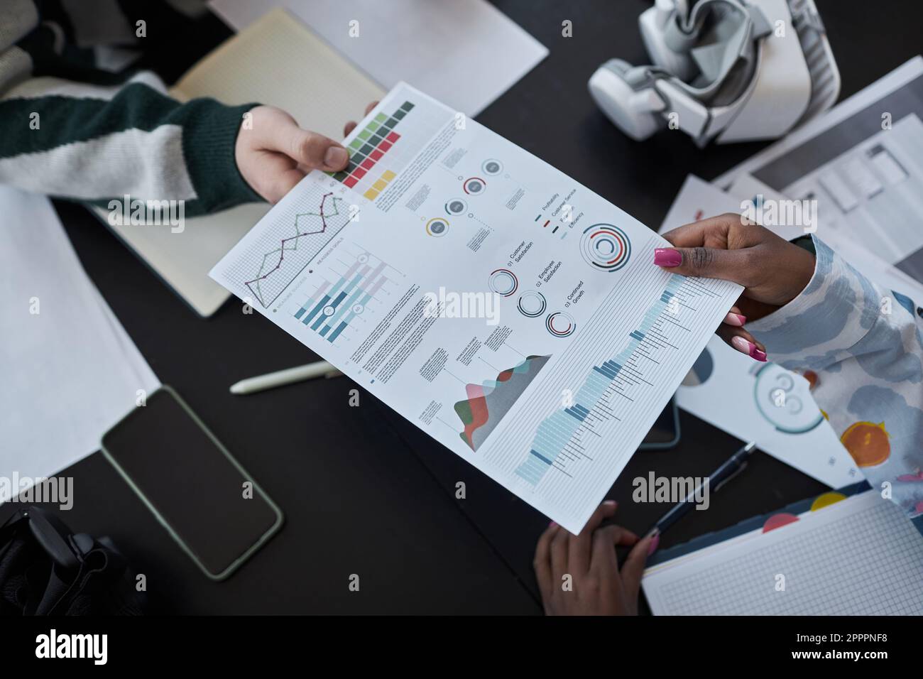 Vista ad alto angolo dei colleghi che esaminano il documento con grafici a tabella durante la riunione in ufficio Foto Stock
