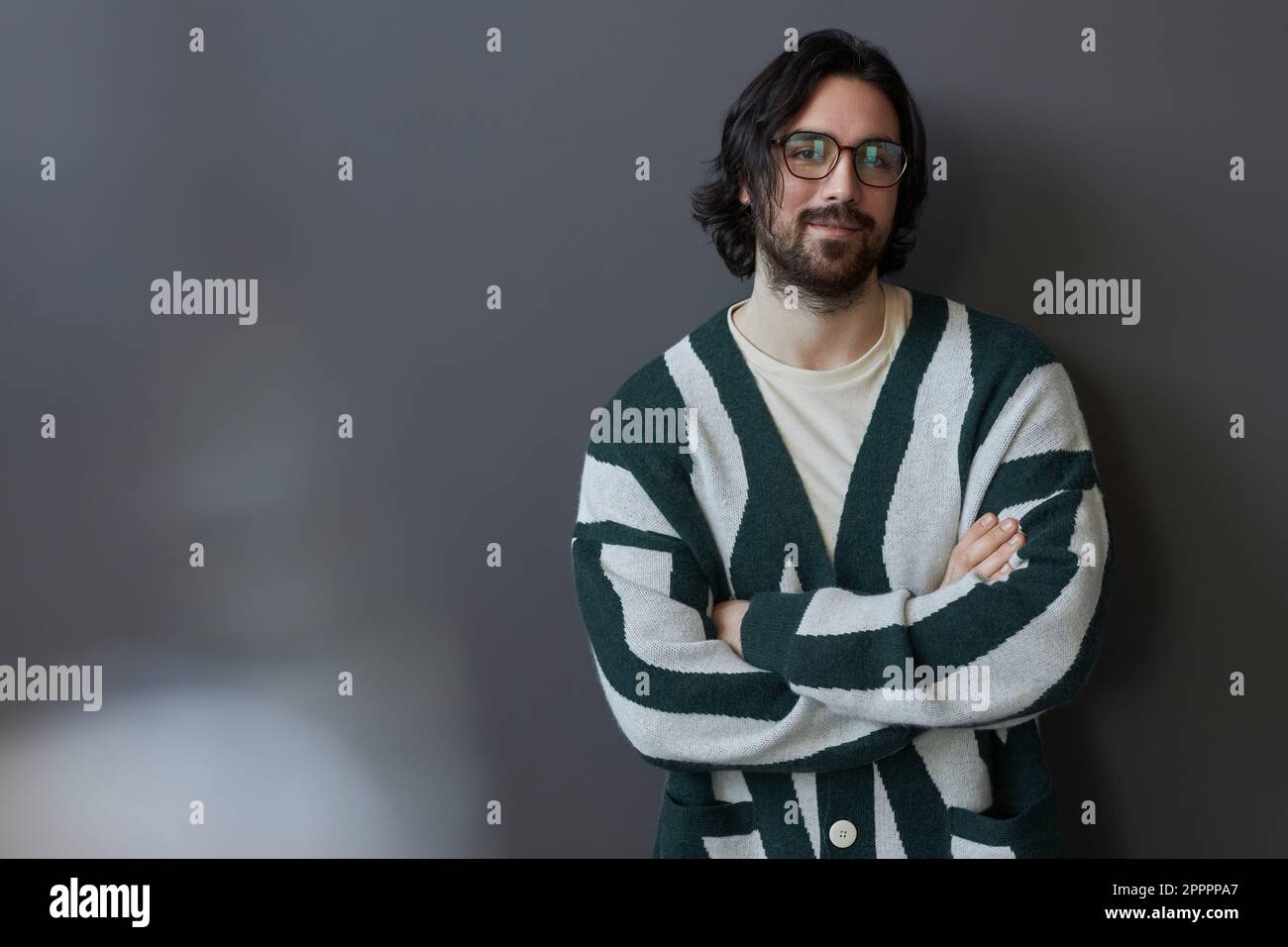 Ritratto di giovane uomo bearded in occhiali e maglione guardando la macchina fotografica in piedi su sfondo grigio Foto Stock