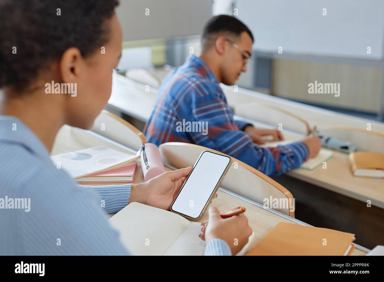 Studente che si stacca dallo smartphone seduto al tavolo con libri durante l'esame all'università Foto Stock