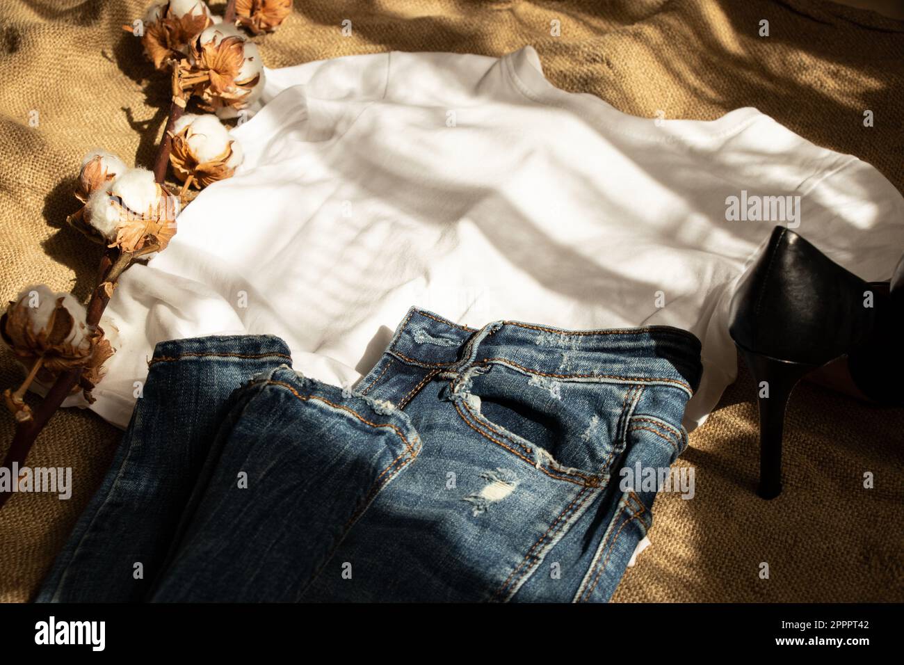 T-shirt e jeans bianchi si trovano su una tela marrone e un ramo di cotone e scarpe, abiti di moda e scarpe per le donne Foto Stock