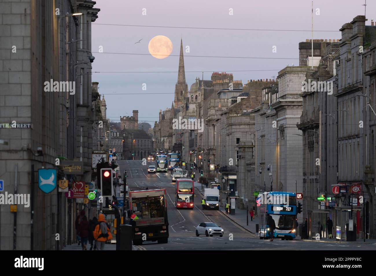 Guardando verso ovest lungo Union Street nel centro di Aberdeen come la Luna piena si trova dietro Gilcomston Church spire presto una mattina di aprile Foto Stock