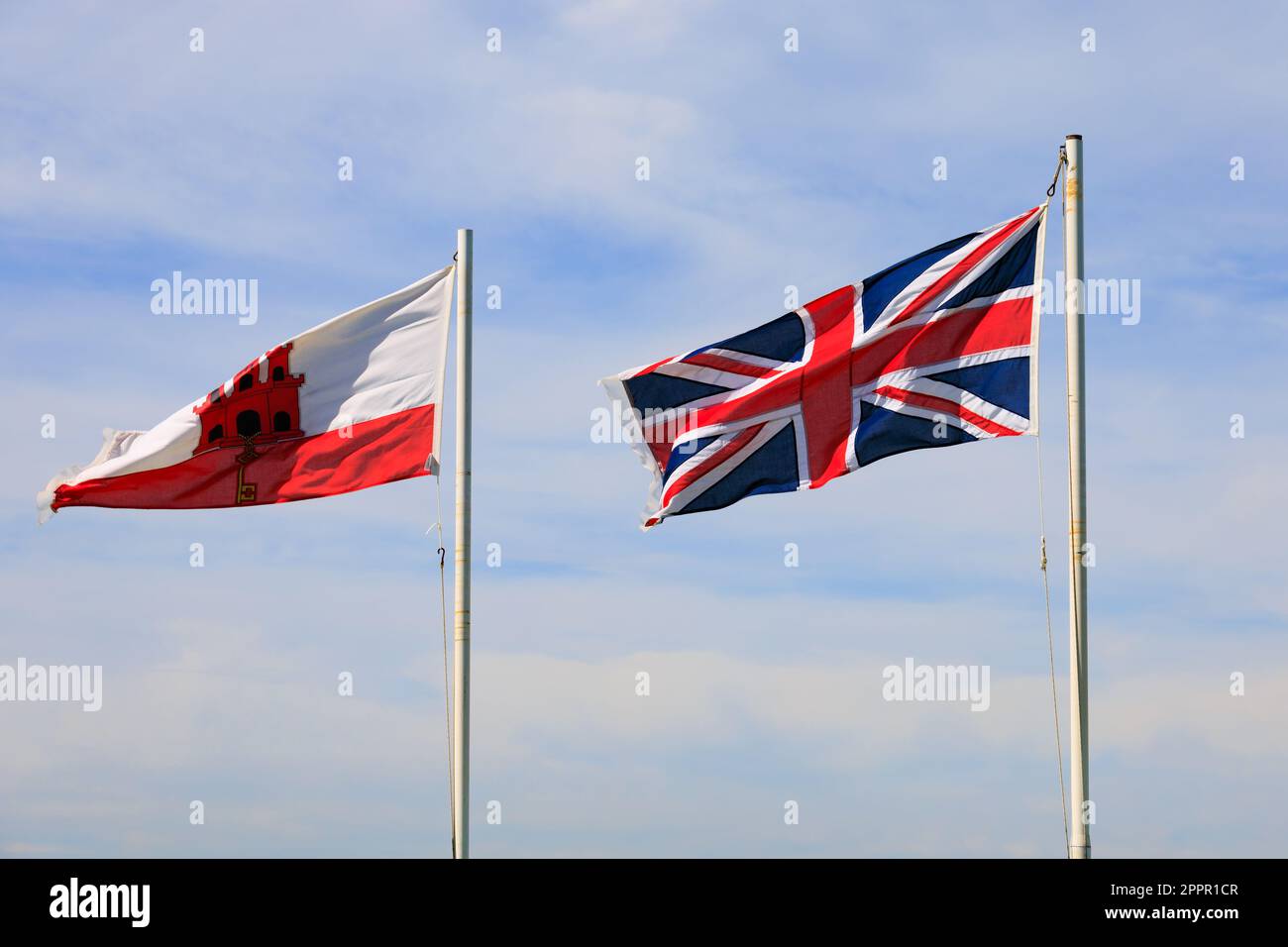Bandiera di Gibilterra e Union Jack che volano fianco a fianco. Il territorio britannico d'oltremare di Gibilterra, la roccia di Gibilterra sulla penisola iberica. Foto Stock