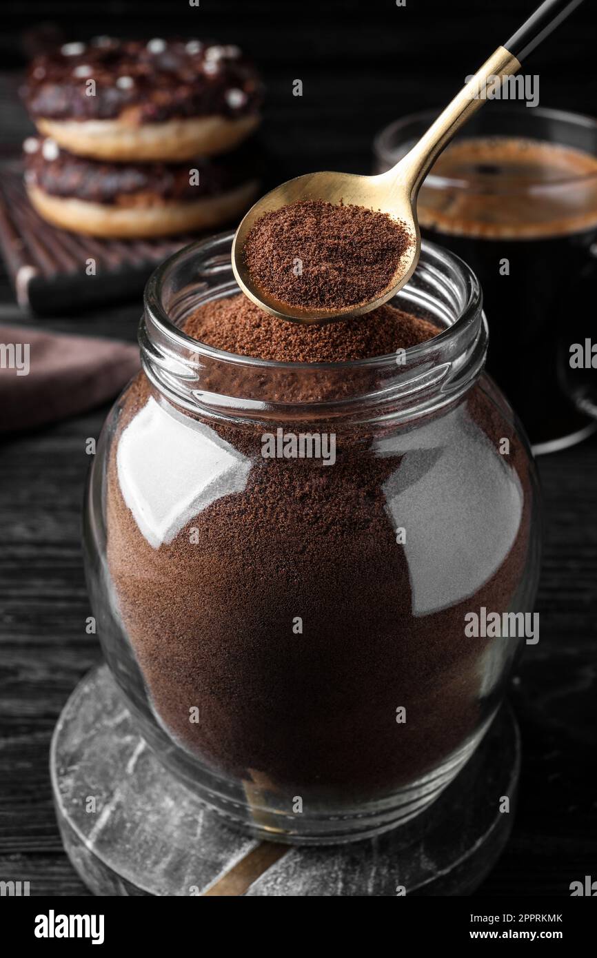 Cucchiaio di caffè istantaneo sopra il vaso su un tavolo di legno nero Foto Stock