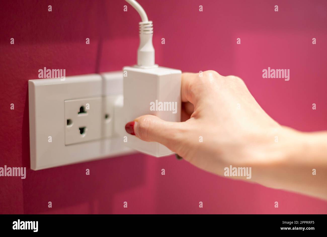 La mano è scollegate la linea elettrica da una presa bianca sulla parete rossa. Foto Stock