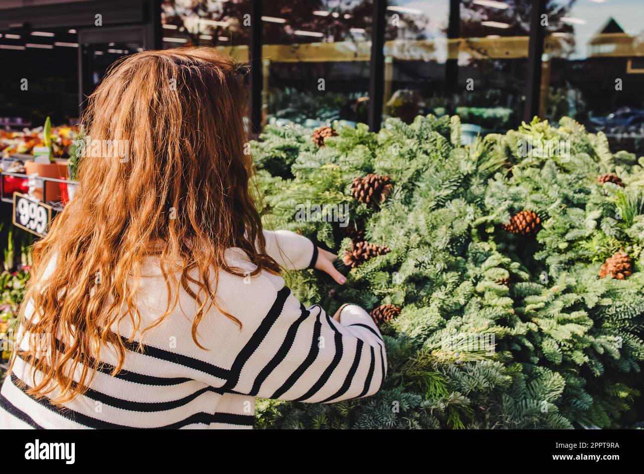 Donna che sceglie una corona decorativa di Natale per acquistare al negozio o al mercato all'aperto Foto Stock