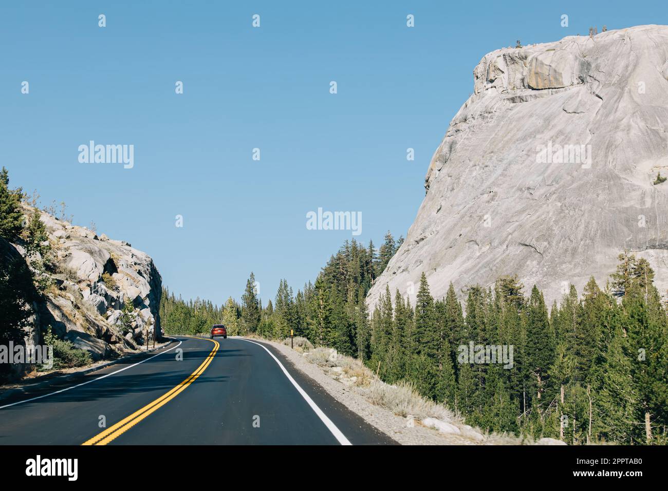 Strada attraverso le montagne con una macchina rossa a distanza in una giornata di sole Foto Stock