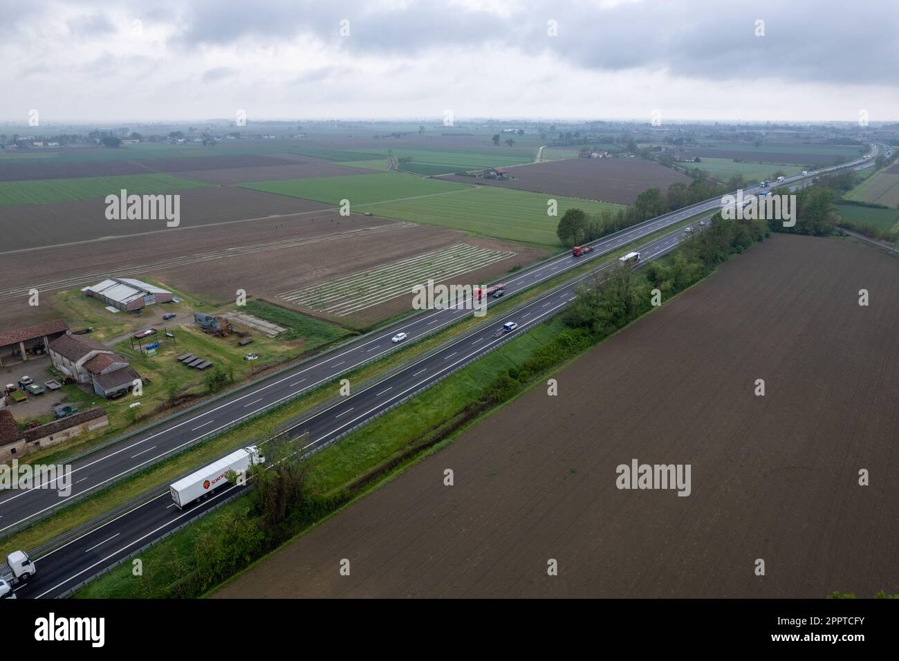 Piacenza, Italia - Aprile 2023 autocarri e auto da carico in autostrada del sole A1 punto di vista aereo tra pianura padana e campi rurali Foto Stock