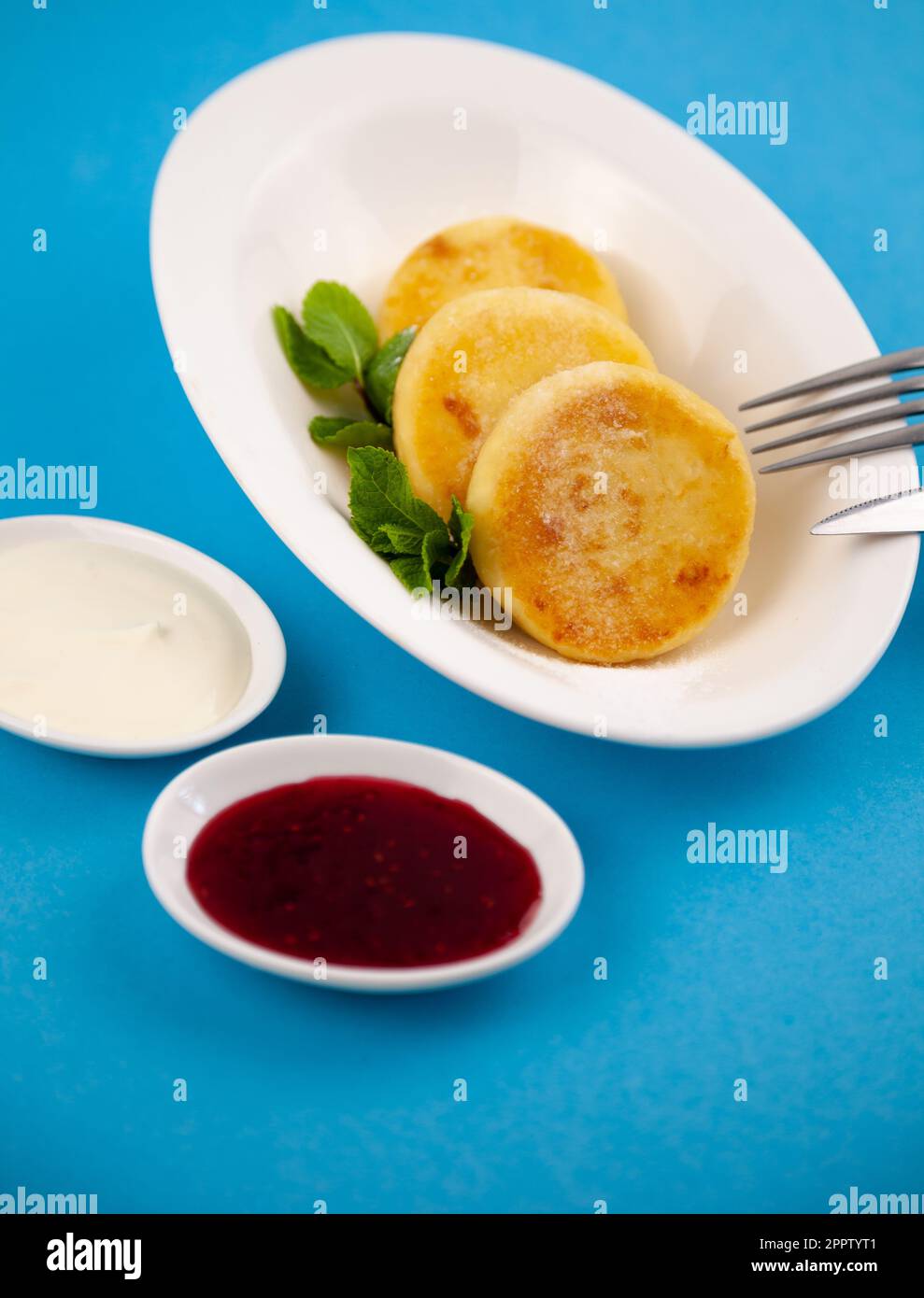 Frittelle di formaggio ricotta rotonda in un piatto bianco su sfondo blu. Cibo prima colazione. Cibo sano. Salsa di panna acida e menta. Primo piano vista dall'alto. Pasto dessert. Frittelle di ricotta al formaggio ricotta. Foto Stock