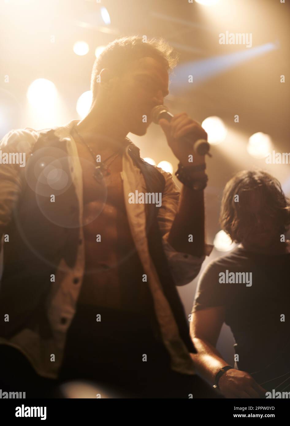 Cantante da palco, leggera e maschile con microfono sul palco o .rock and roll star durante il concerto notturno. Band, musica e festival per karaoke o creativi Foto Stock