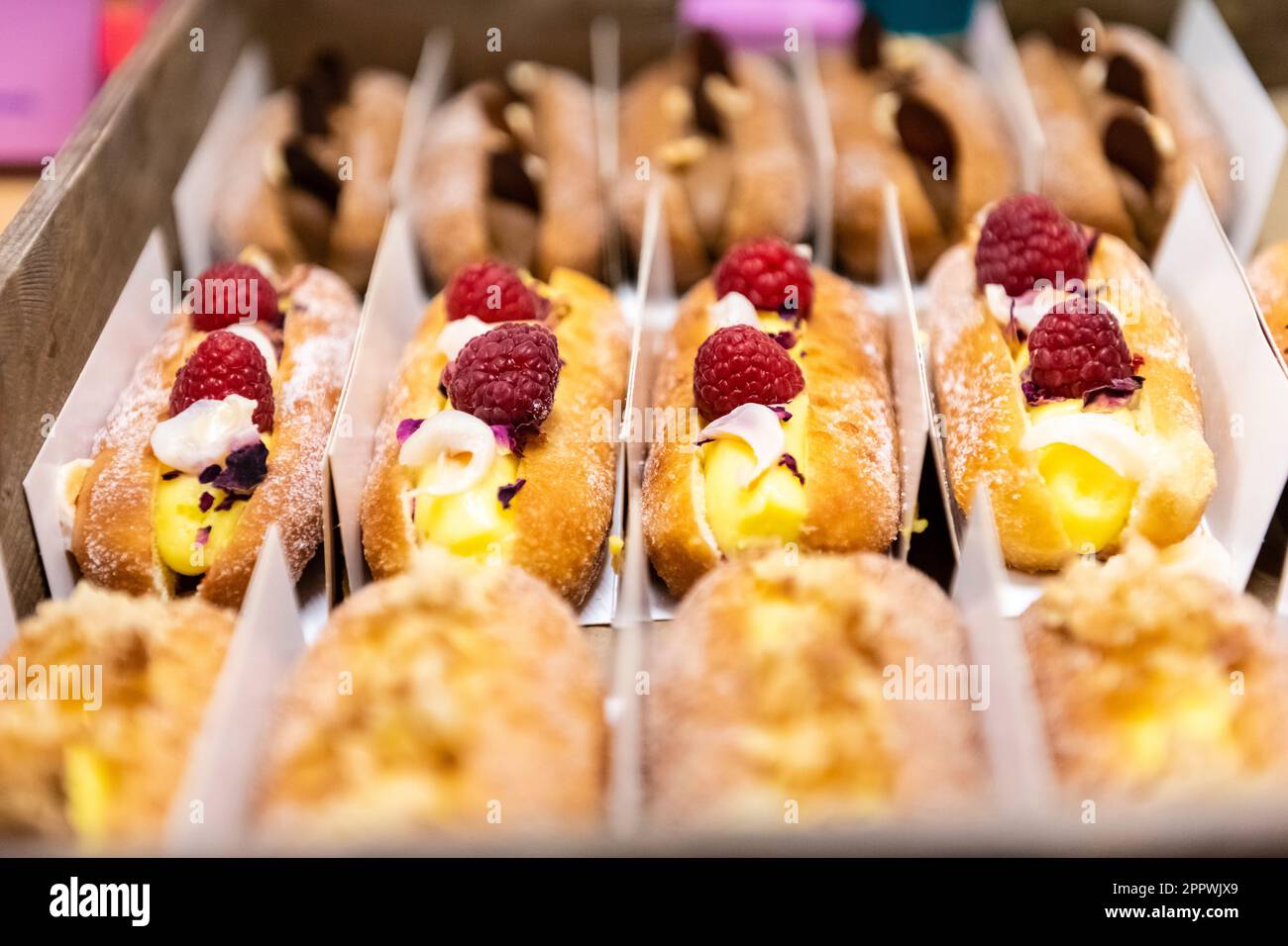 Primo piano di una bella e vivace esposizione di pasticcini francesi attraverso una finestra di panetteria, ciambelle aperte Foto Stock