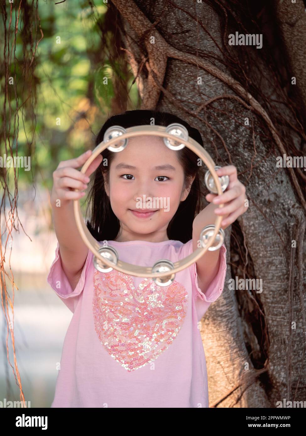 Bambina asiatica giocare il tamburello, nel giardino sotto il grande albero Foto Stock