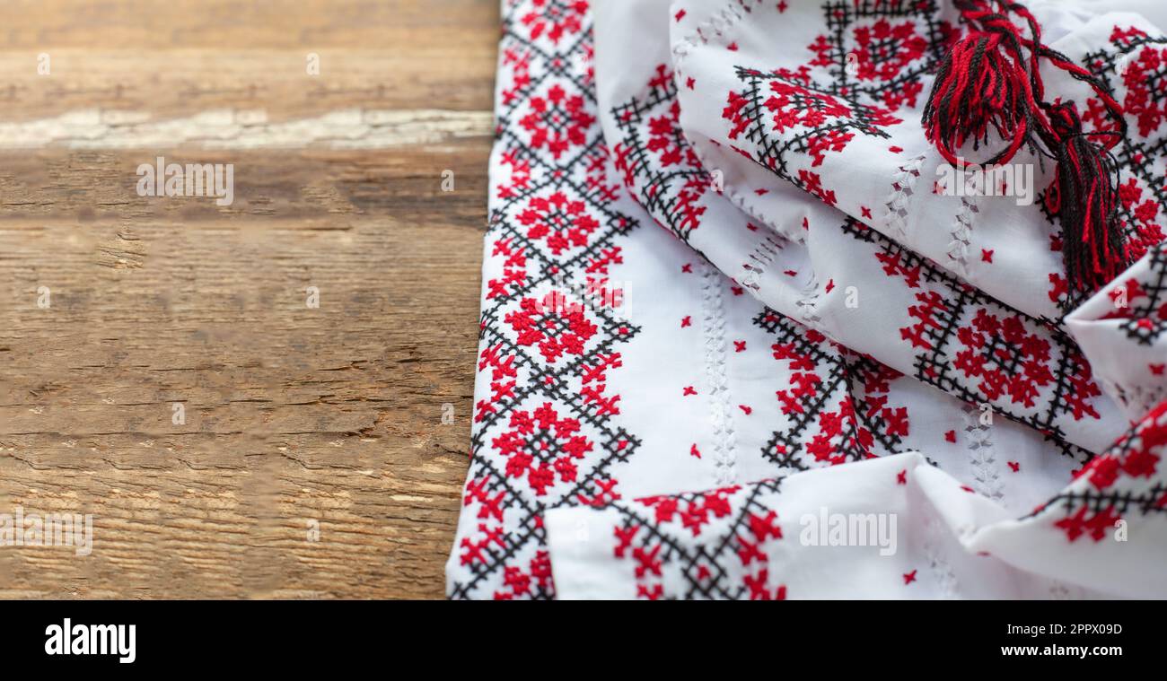 Maglietta bianca ricamata con abiti ucraini. Fili rossi e neri su sfondo di legno. Vyshyvanka è un simbolo dell'Ucraina. Spazio copia ricamo. Cuciture incrociate. Foto Stock