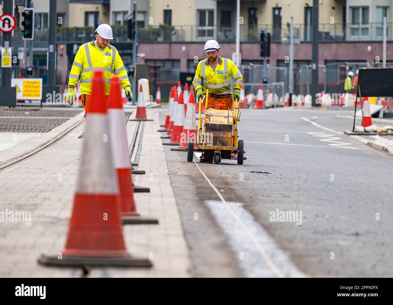 Due operai dipingono linee bianche sulla strada accanto ai binari del tram, Leith, Edimburgo, Scozia, Regno Unito Foto Stock