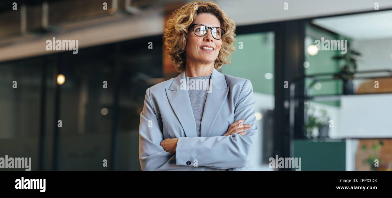 Donna d'affari premurosa in piedi con braccia incrociate. Donna nel suo 40's che lavora in un ufficio. Donna professionista che indossa un abito. Foto Stock