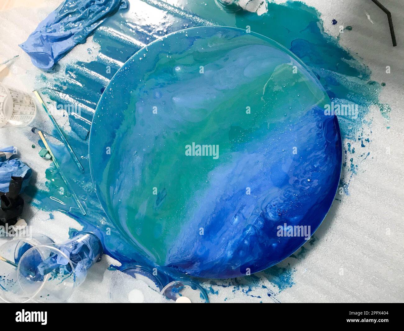 Il processo di creazione di un disegno moderno astratto fatto in casa dipinto con un pennello di resina multicolore blu acrilico su un asse di legno rotondo Foto Stock