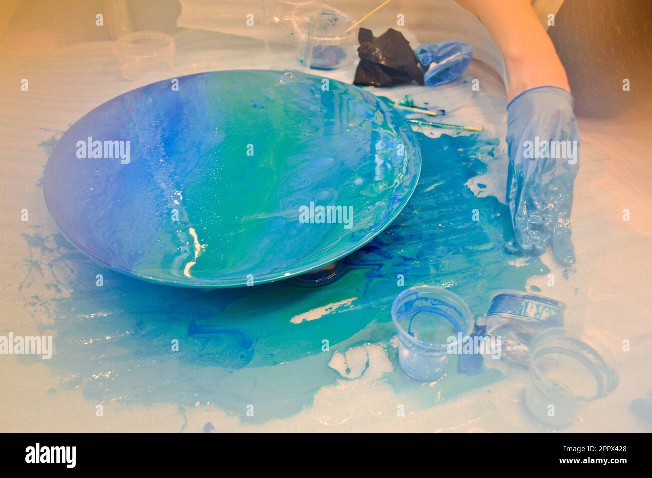 Un uomo in un guanto blu dipinge splendidamente una resina multicolore blu acrilico una tavola rotonda fatta in casa. Foto Stock