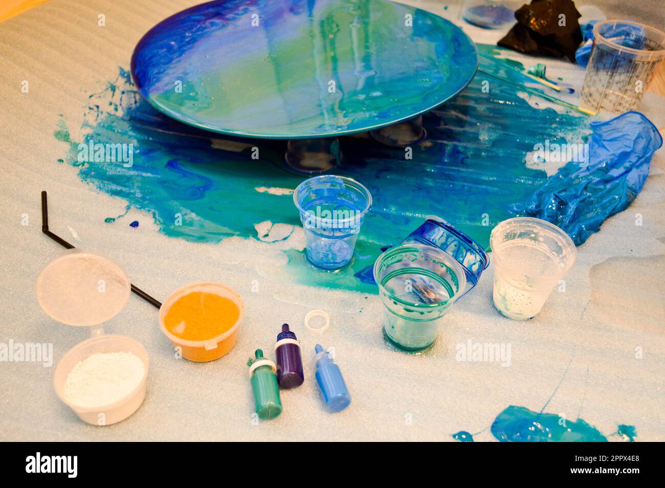 Il processo di creazione di un disegno moderno astratto fatto in casa dipinto con un pennello di resina multicolore blu acrilico su un asse di legno rotondo. Foto Stock
