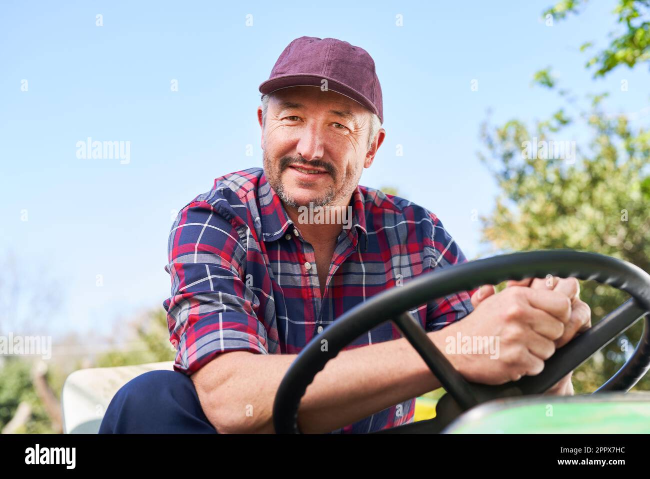 Ritratto di contadino maschio maturo che guida il trattore con cielo limpido sullo sfondo nelle giornate di sole Foto Stock