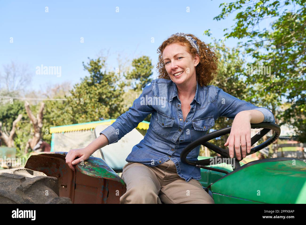 Ritratto di felice contadino maturo seduto su un trattore verde con cielo limpido sullo sfondo durante le giornate di sole Foto Stock