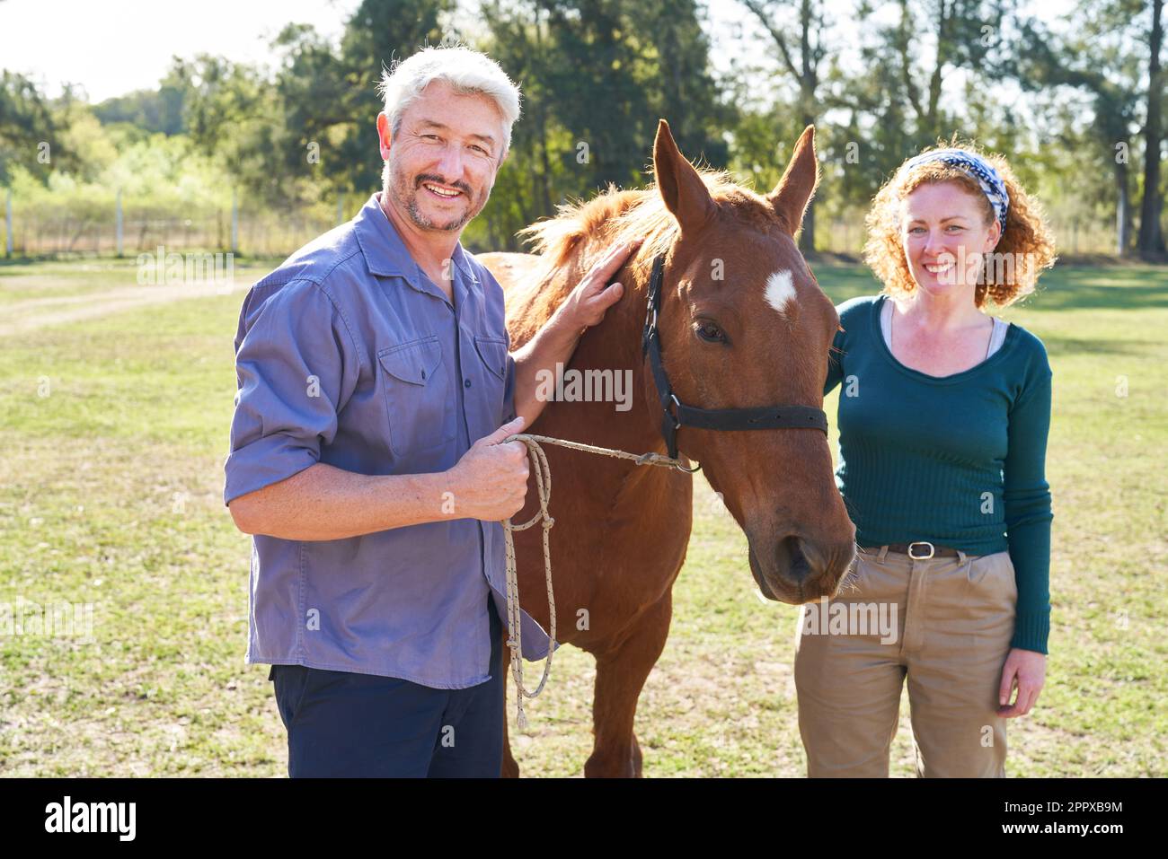 Ritratto di felice uomo e donna che tiene cavallo in ranch fattoria Foto Stock