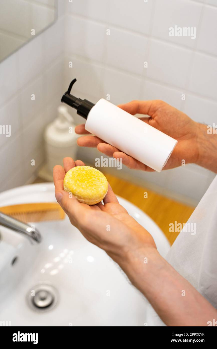 Un uomo sta scegliendo fra una barra solida dello shampoo ed una liquida. Accessori per il bagno. Senza plastica, senza sprechi, ingredienti a basso contenuto di acqua. Foto Stock