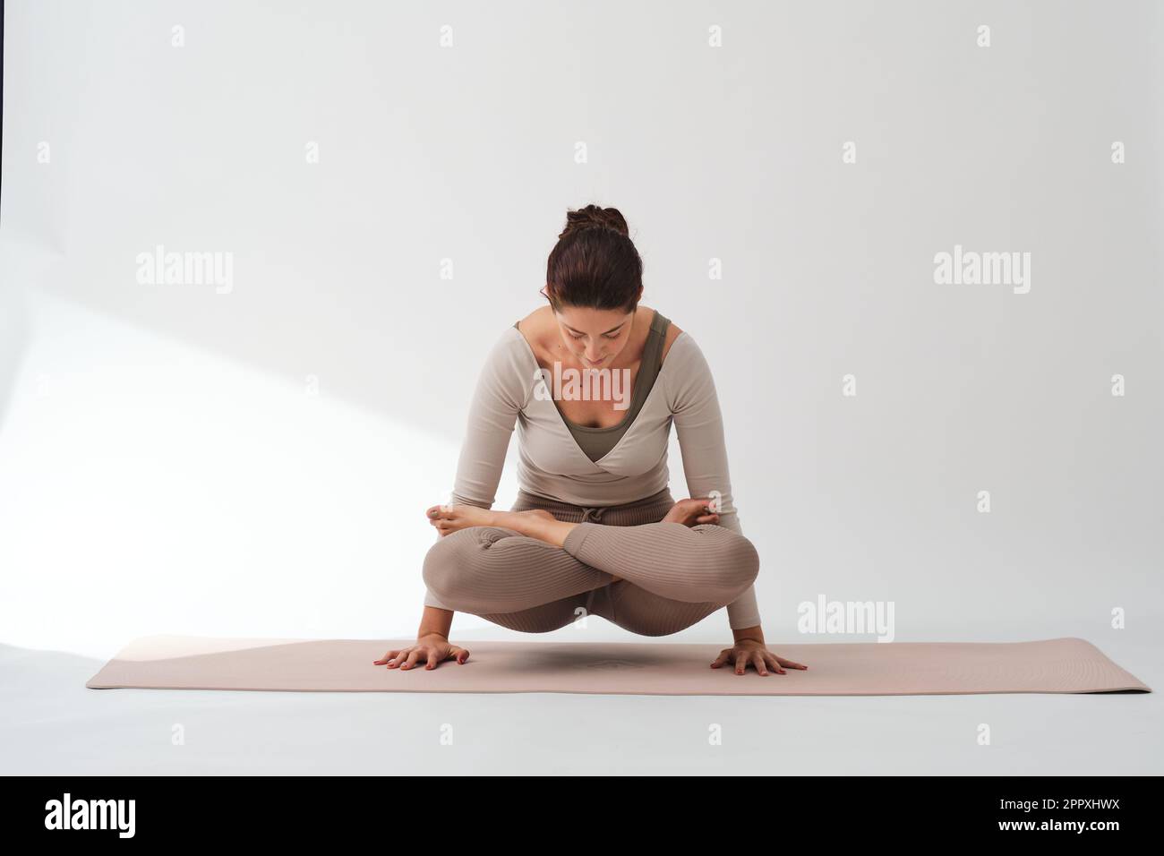 Corpo pieno di scala a piedi nudi posa sul tappetino mentre si allenano contro la parete bianca durante l'allenamento yoga in studio Foto Stock