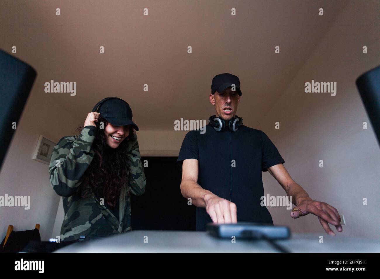 Allegri DJ adulti maschi e femmine in abiti casual che girano pulsanti sulla console di mixaggio mentre creano musica in casa studio Foto Stock