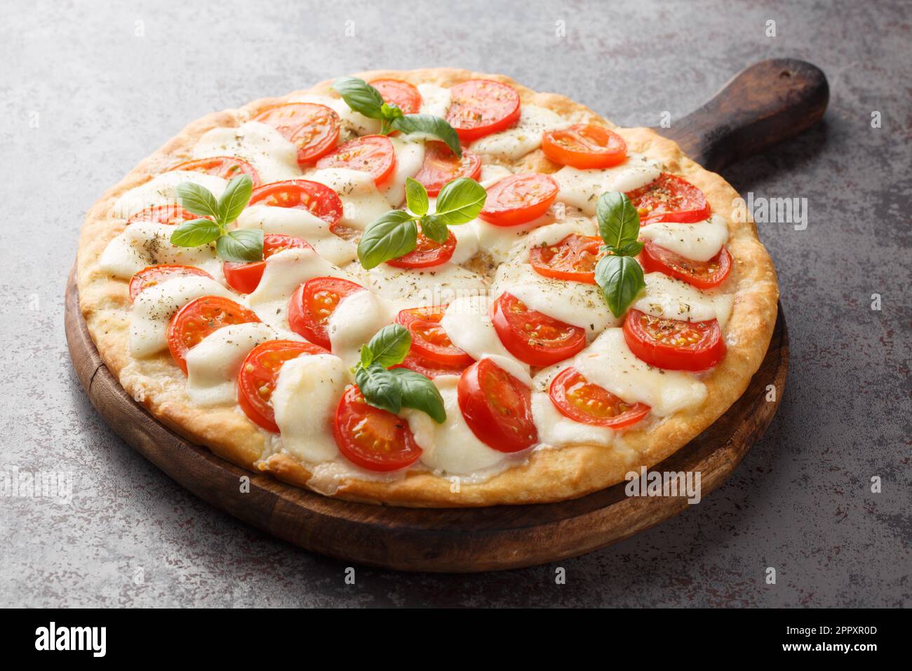 Pizza caprese appena sfornata con formaggio, pomodori e basilico primo piano su un asse di legno sul tavolo. orizzontale Foto Stock
