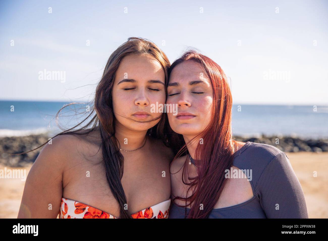 Due sorelle si posano con il volto vicino e gli occhi chiusi alla spiaggia, amore tra le sorelle. Foto Stock