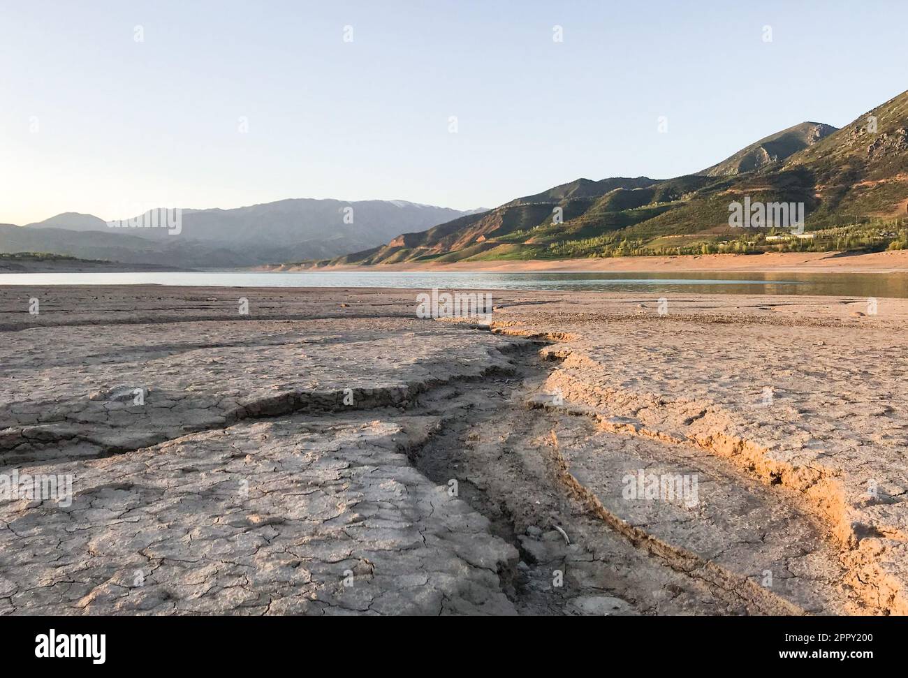 Bel paesaggio con sole tramontato: Montagne, lago, terra cracked con pietre - Dried-up riverbend. Foto Stock