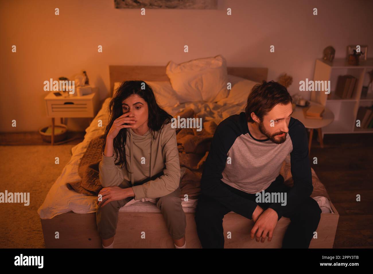 Donna insoddisfatta seduta vicino al ragazzo a letto di notte, immagine stock Foto Stock