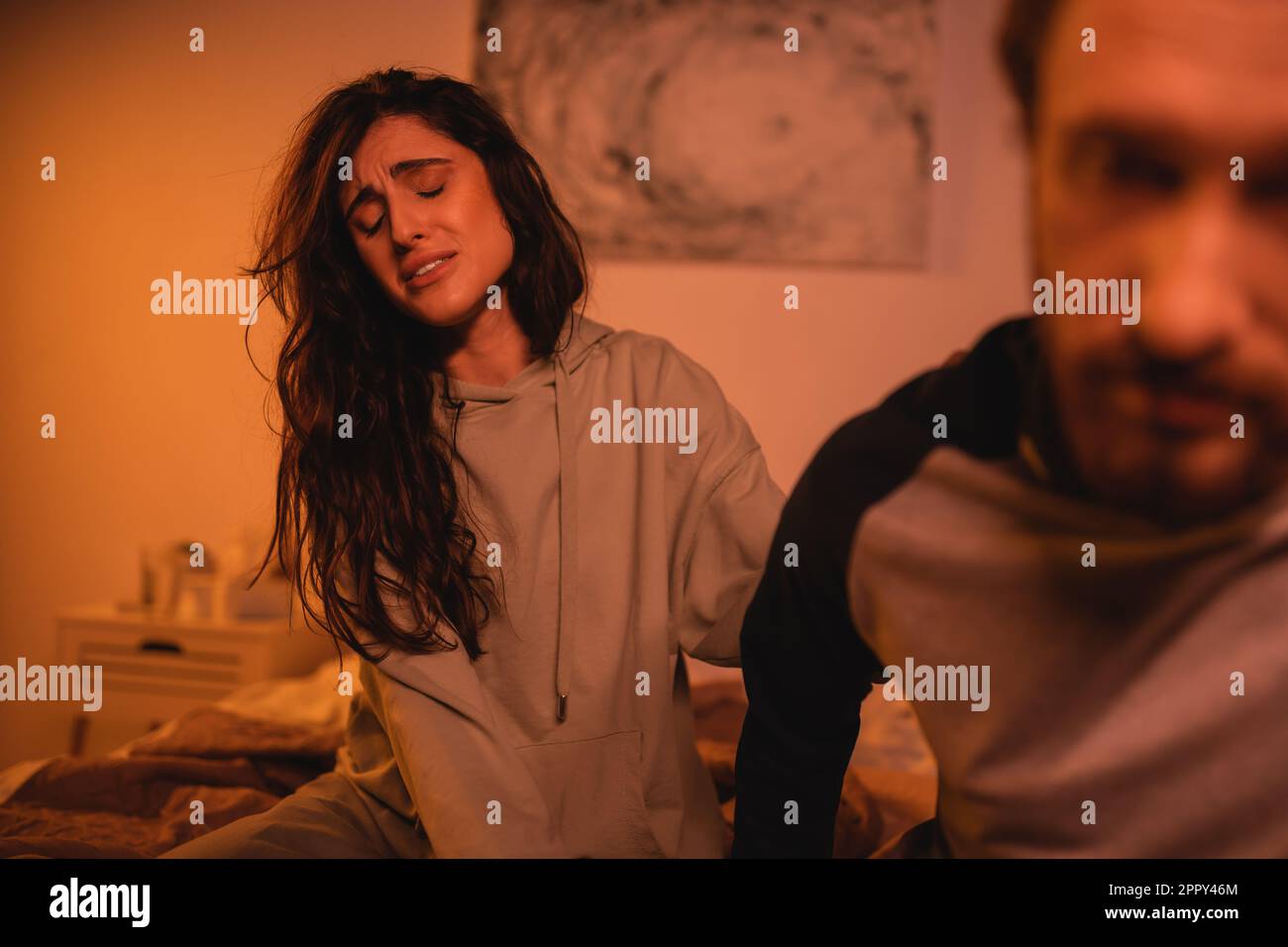 Donna insoddisfatta seduta vicino boyfriend sfocato in camera da letto di notte, immagine di scorta Foto Stock