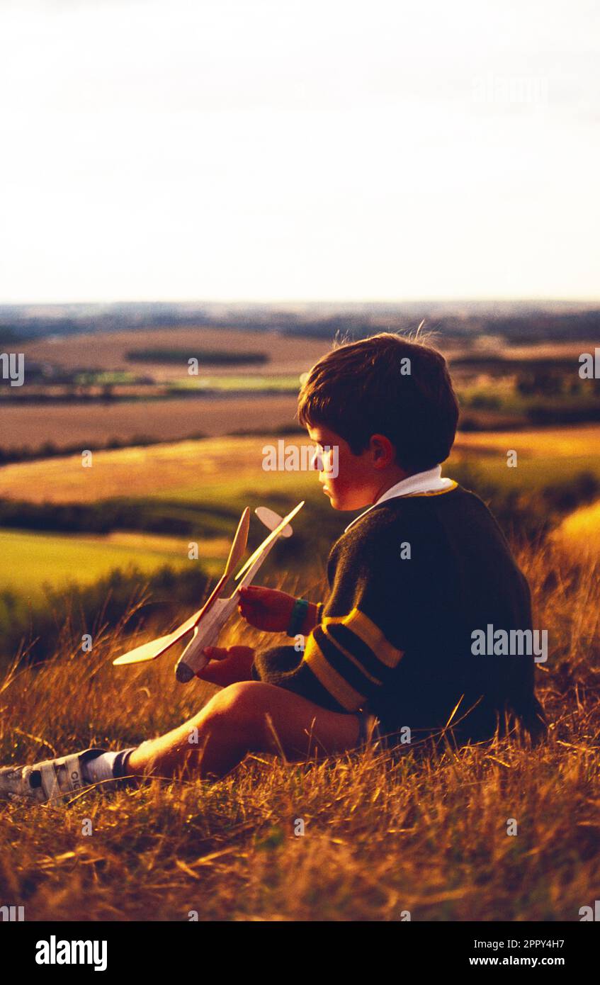 Inghilterra. Bambini. Ragazzo seduto su una collina con il suo modello di aereo. Foto Stock