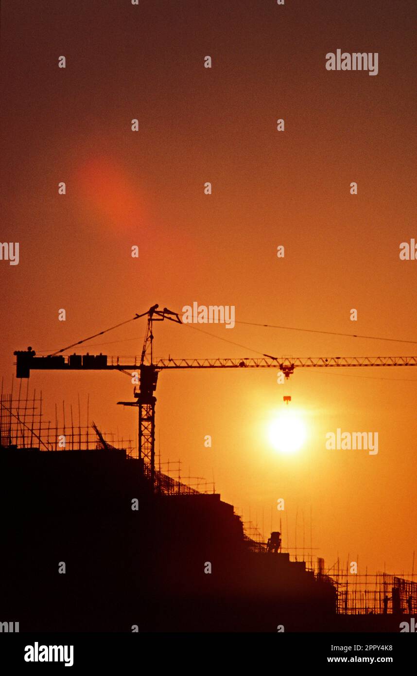 Cina. Hong Kong. Tramonto. Silhouette di gru alta sopra l'edificio in costruzione. Foto Stock