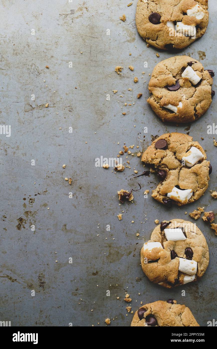 I biscotti di marshmallow s'mores a base vegetale e vegana in una linea sul lato destro di una teglia da forno d'annata Un biscotto ha un morso preso da esso. Foto Stock