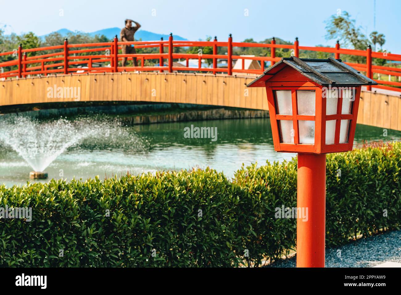 Splendida vista delle lampade all'aperto sulla passerella per l'illuminazione del giardino nel parco estivo con immagine sfocata del ponte rosso sullo sfondo. Sentiero nel parco con il Foto Stock