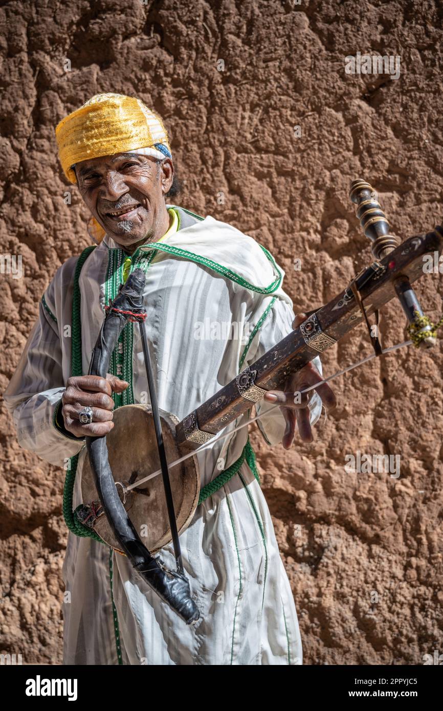 Uomo vestito in tipico costume berbero che suona uno strumento a corde, noto come Ribab, nei vicoli della Kasbah Taourirt. Foto Stock