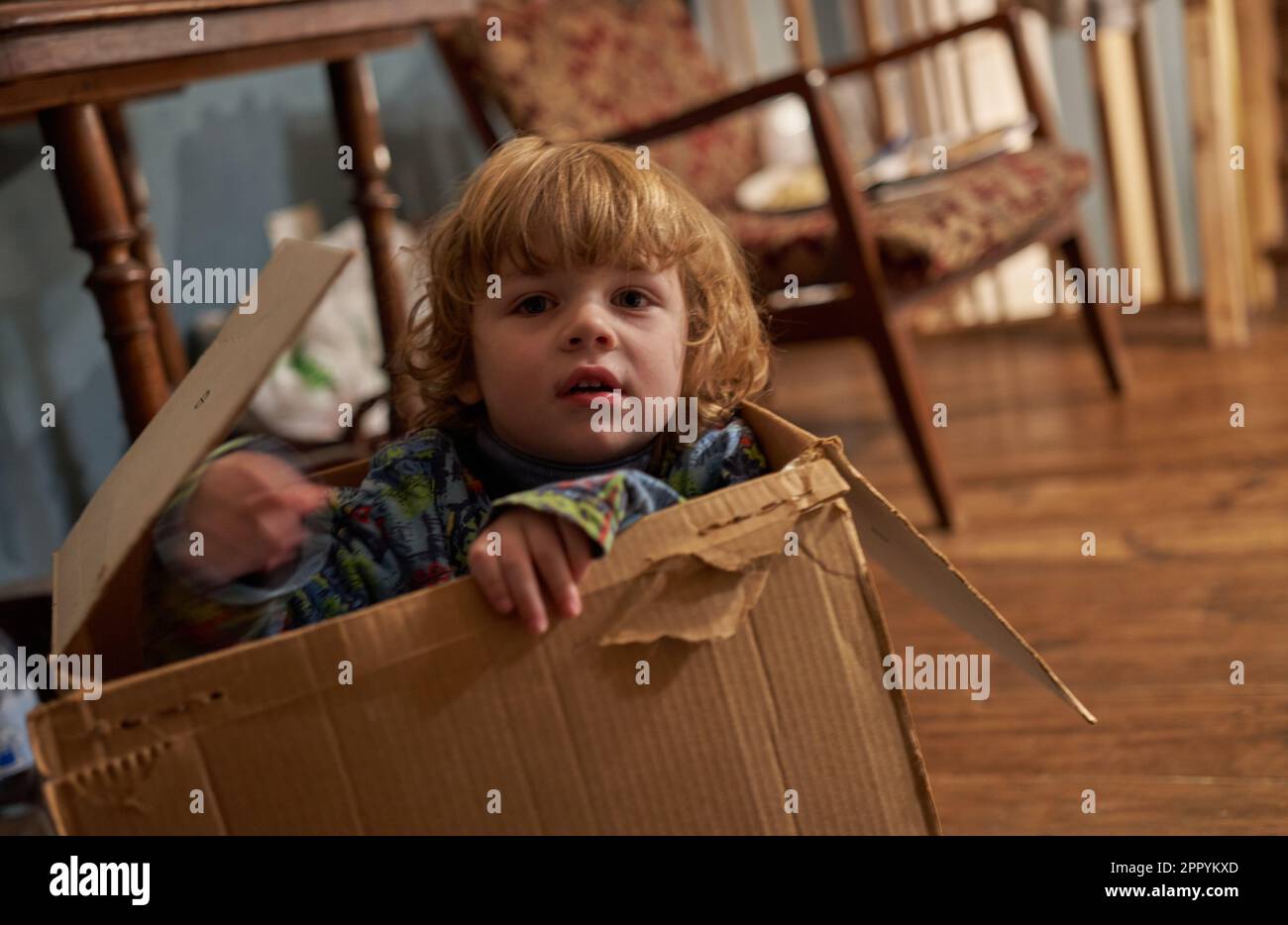 Un ragazzino guarda fuori da una scatola di carta e sorride Foto Stock