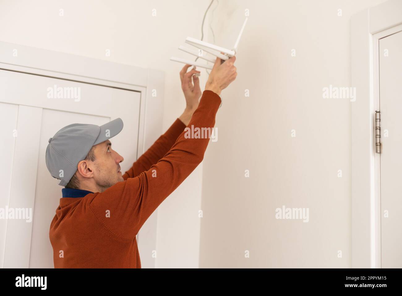 Un lavoratore installa un router sulla parete per trasmettere il segnale Internet in uffici e case, vista laterale Foto Stock
