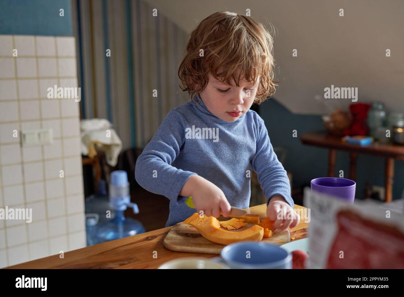 Un ragazzino lavora in cucina, taglia una zucca Foto Stock