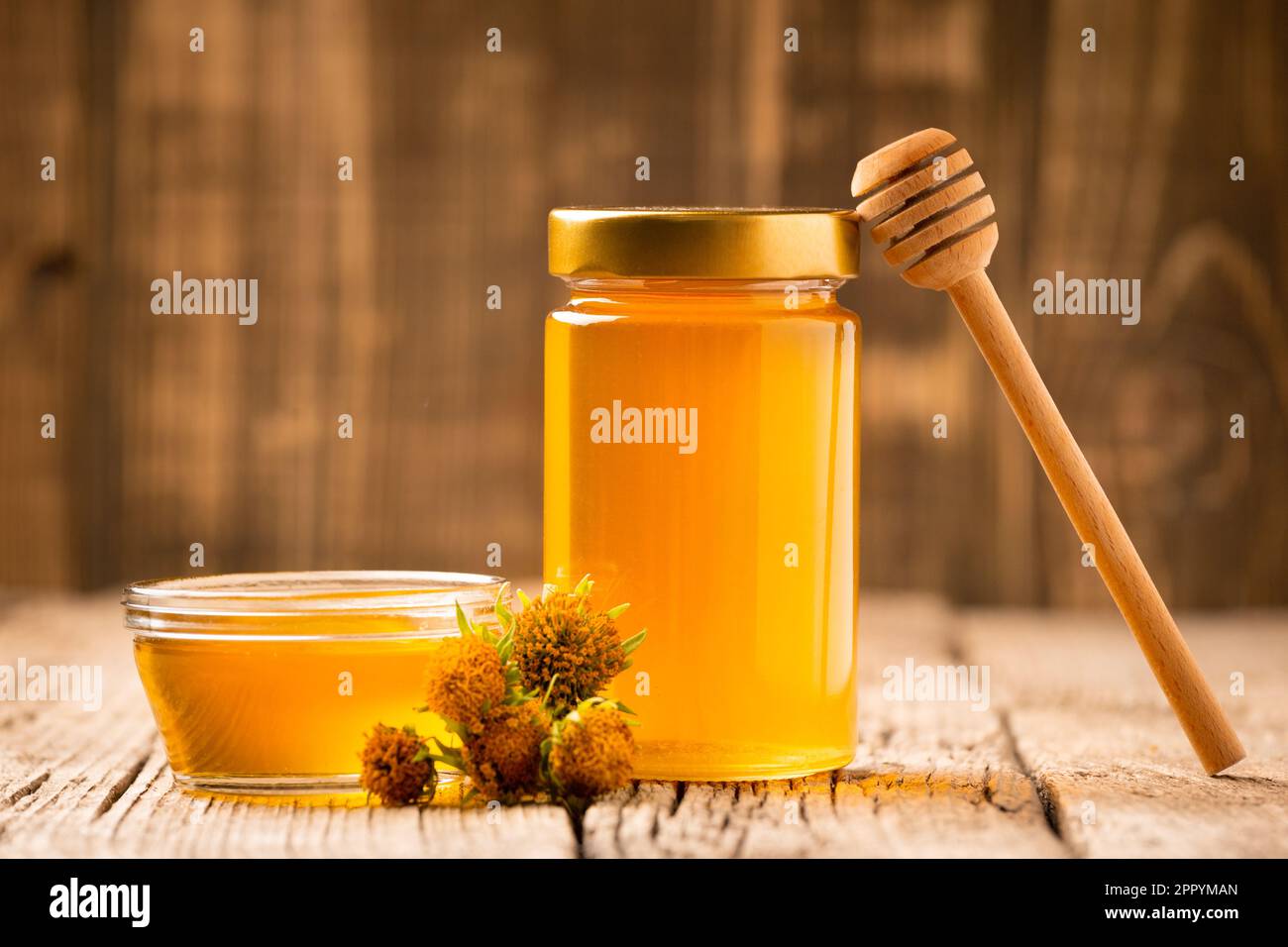Composizione creativa di miele in un vaso di vetro e una ciotola, un divanetto di legno e fiori gialli su un vecchio sfondo di legno. Foto Stock