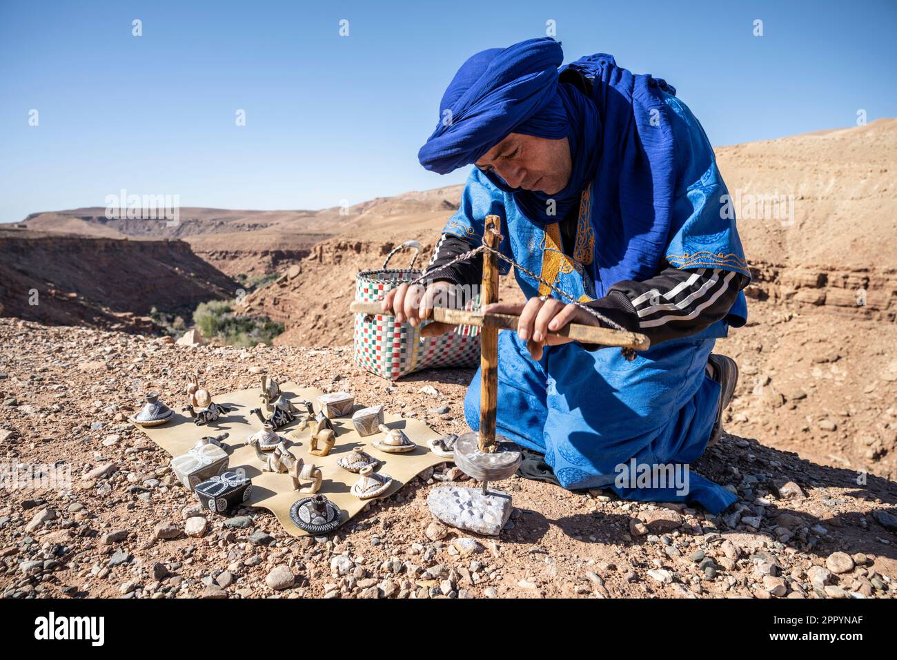 Artigiano vestito in tipico abito berbero lavorando la pietra con un trapano manuale. Foto Stock