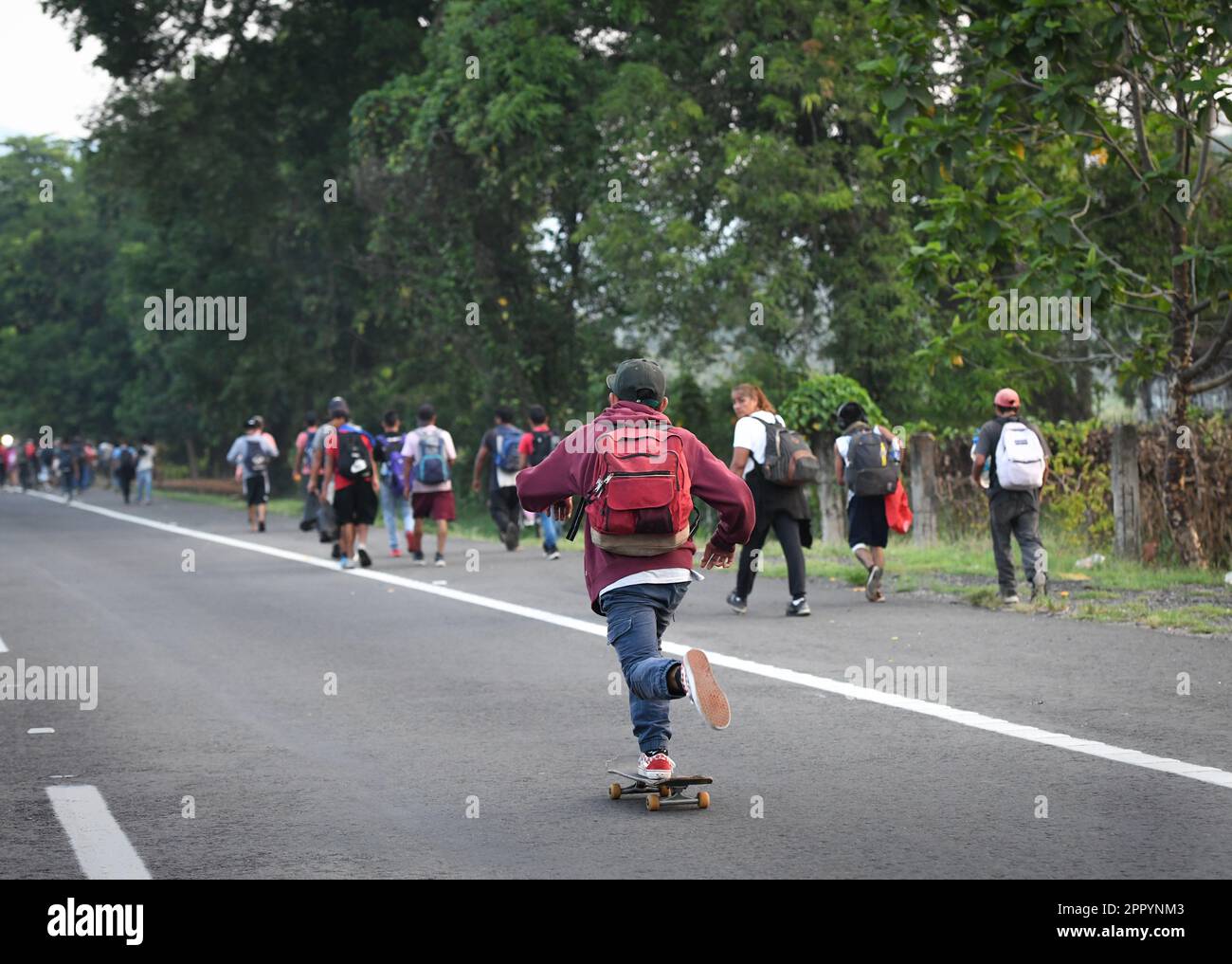 Huehuetan, Messico. 25th Apr, 2023. Un giovane migrante pattina un po' mentre altri migranti marciano a piedi lungo un'autostrada. Le circa 3.000 persone, soprattutto dell'America centrale, che si sono insediate a nord domenica, vogliono richiamare l'attenzione sulla loro situazione e chiedere giustizia dopo la morte di 40 migranti in una struttura per l'immigrazione. Credit: Isaac Guzman/dpa/Alamy Live News Foto Stock