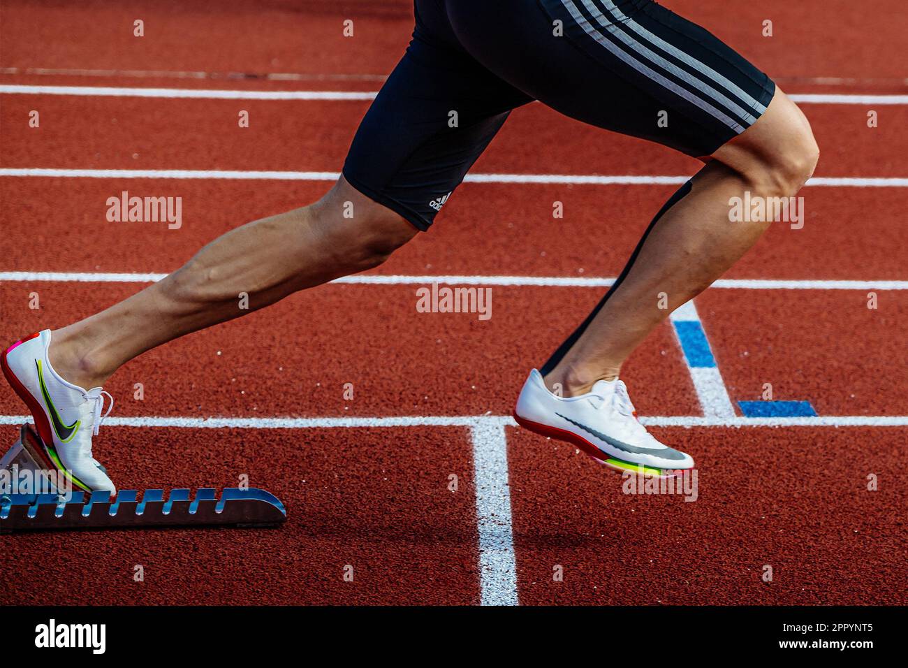 Le gambe in primo piano indossano scarpe Nike Spikes e tights Adidas e iniziano a correre dai blocchi di partenza dello stadio Red Track Foto Stock