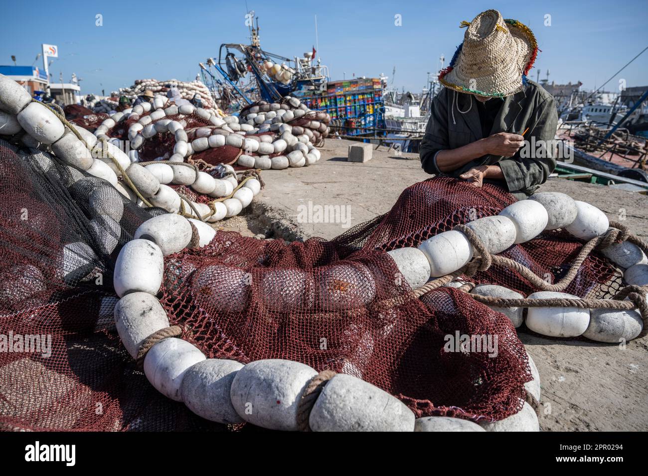 Pescatore riparazione reti da pesca nel porto di Essaouira. Foto Stock