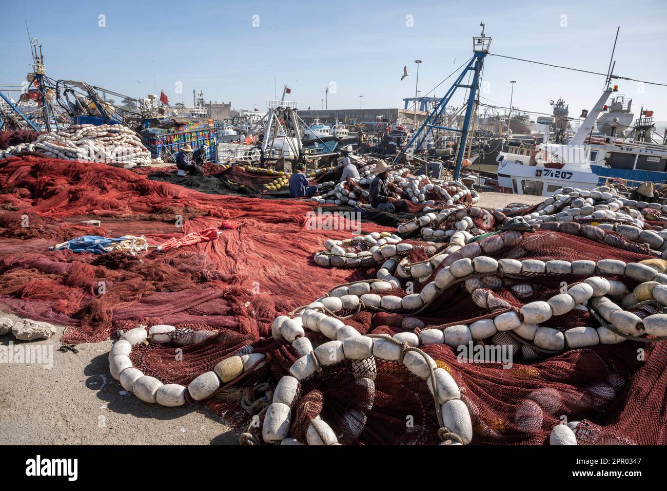 Pescatori che riparano reti da pesca nel porto di Essaouira. Foto Stock