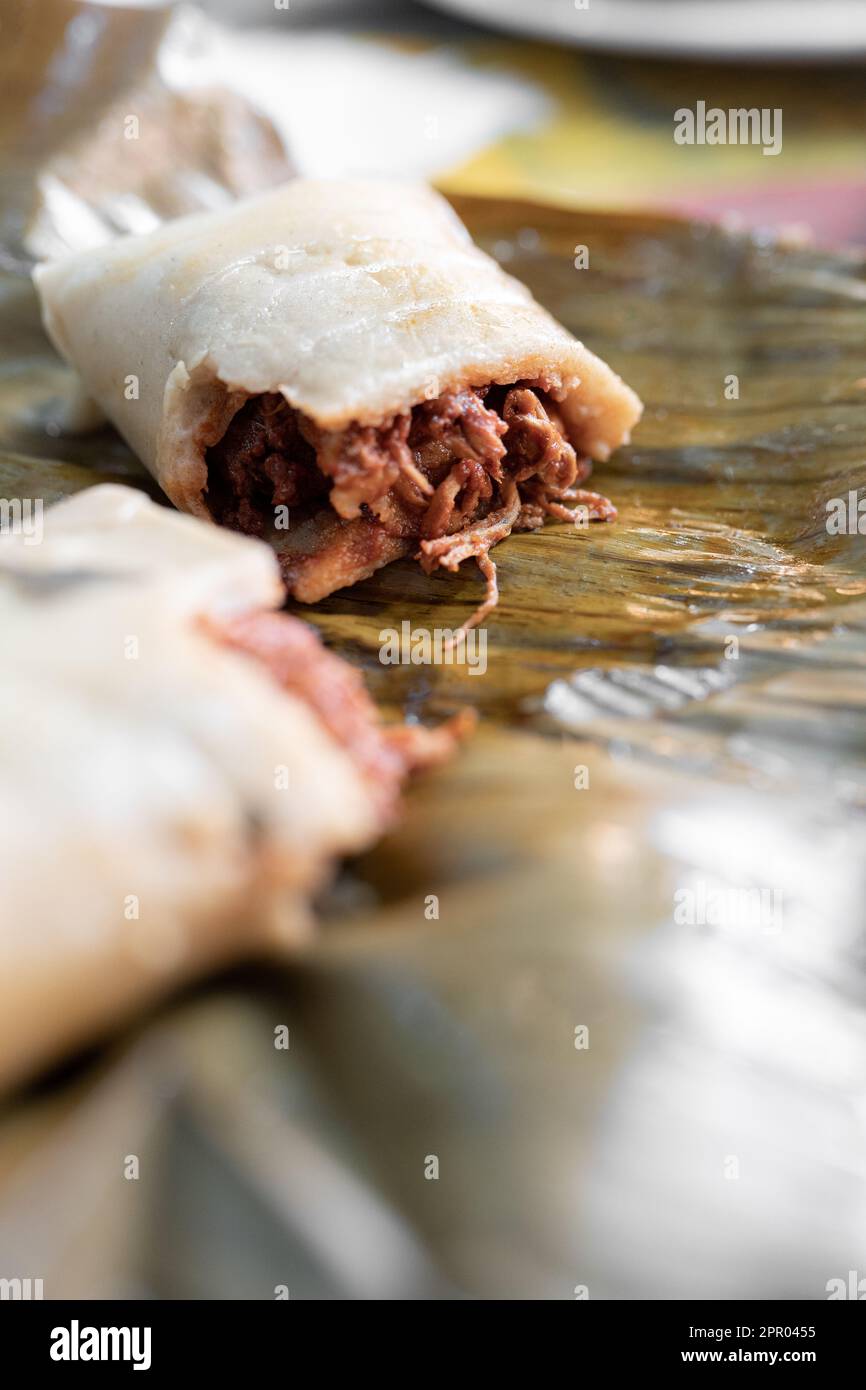 Primo piano di un tamale di carne appena cucinato tagliato a metà su una foglia di pianta Foto Stock
